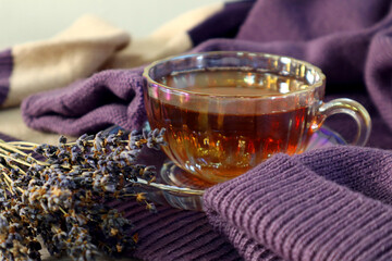 A bouquet of dry lavender next to a cup of hot tea on a pastel knitted sweater, close-up