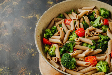 delicious penne wheat pasta with tomatoes, broccoli and mozzarella on a dark background