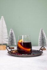 Mulled wine with orange in a glass on a plate on grey and green background.