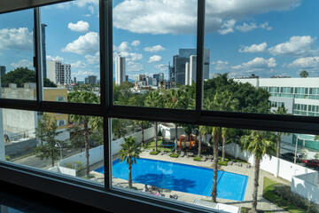 view of a swimming pool from an apartment up in a tower, view of buildings, trees and palm trees