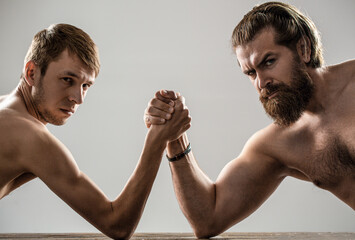 Arm wrestling. Heavily muscled bearded man arm wrestling a puny weak man. Arms wrestling thin hand,...