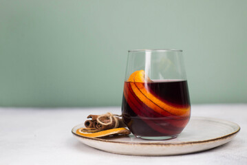 Mulled wine with orange in a glass on a plate on grey and green background.