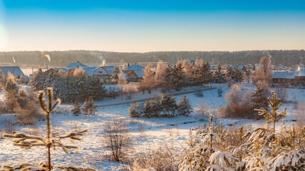 Winter landscape with snow-covered trees, houses in the background of blue sky