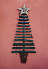 Handmade craft Christmas tree made from wooden planks and illuminated garland as outdoor wall decoration. Xmas upcycling handicraft design