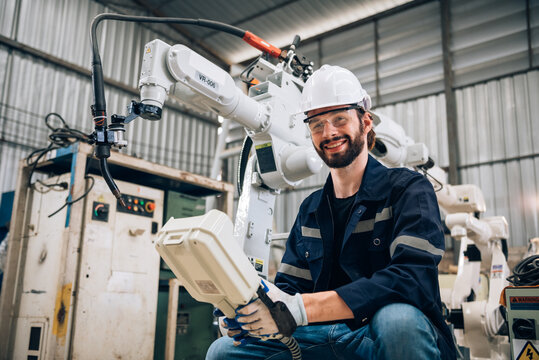 Caucasian man specialist engineer in uniform smiling and holding robotic arm controller for working in smart industrial factory. - Powered by Adobe