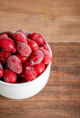 Frozen dogwood on a wooden background. Freshly frozen dogwood berry for compote, juice. vertical photo