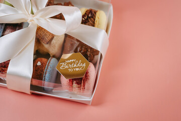 Gift box with juicy large macaroons. Decorated with a bow and the inscription happy birthday. On a pink background.