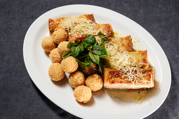 Fried cheese balls, and potato lasagna, on a white plate, decorated with herbs and cheese. Concept of restaurant, food.