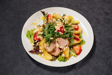 Salad with duck and pear on a white plate, decorated with almond shavings and berries. Restaurant concept.