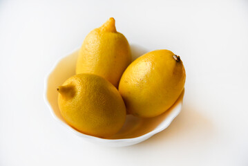 Yellow juicy lemons in a white saucer. Delicious yellow lemons on a white background. Beautiful lemons on a plate.