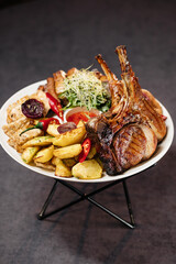 Meat on the bone, grilled chicken breast and veal, with potatoes and sweet and sour sauce, garnished with chili pepper and herbs. Restaurant concept.