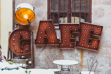 Cozy cafe, rusty signboard with bulb lights and vintage spotlight in Riga old town, Latvia, in...
