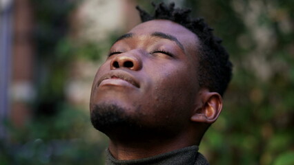 Thoughtful black African man looking up at sky closing eyes in contemplation