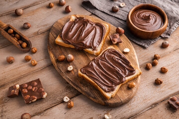 Board of bread with chocolate paste and hazelnuts on wooden background