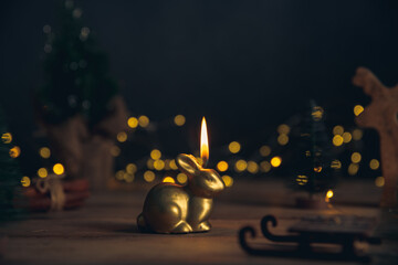 candle in the form of a rabbit symbol of 2023 among the lights, garlands, Christmas trees, chinese...