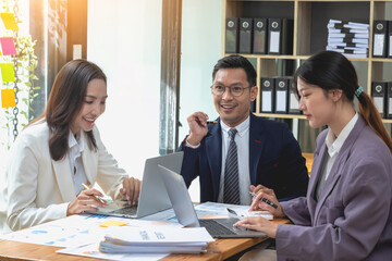 A team of businessmen plan with their laptops and graph charts for their profits and use a calculator to calculate their company is annual balance.