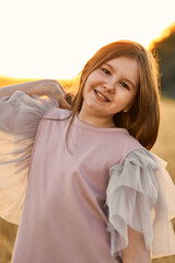 Portrait of pretty smiling girl with long hair in the field in sunset at a summer evening. Healthy summer activity for children. Having fun. Vertival.