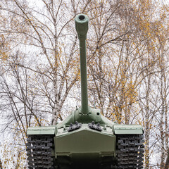 Military green tank on caterpillars with a cannon in front close-up from below background white birches.