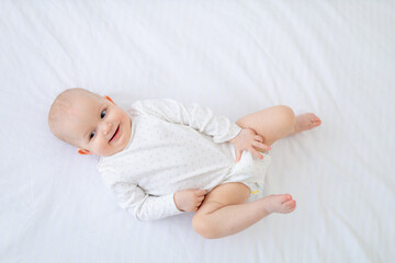 a baby girl of six months lies on her back on a white cotton bed on her back in a bed at home and smiles