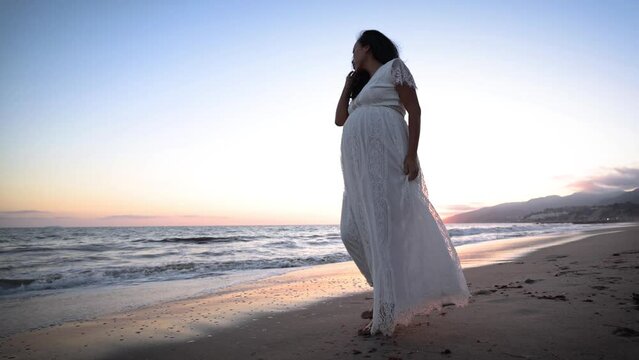 Attractive pregnant Asian woman enjoys a walk on the beach.