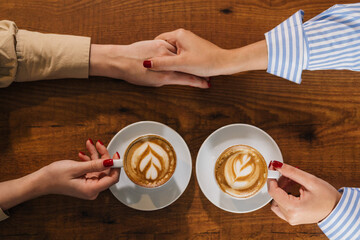 View from above of holding hands and coffee cups