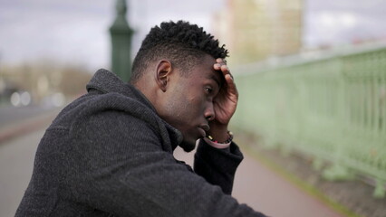 Preoccupied black African man sitting at city street curb feeling anxiety4