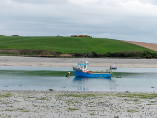 An boat in shallow water. Hills under sky. Silt and seaweed. Landscape.