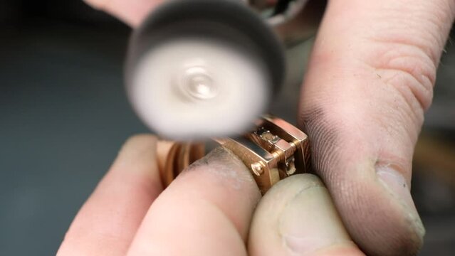 Hands of the jeweler polishes ring on the polishing machine. Goldsmith working on his workbench.