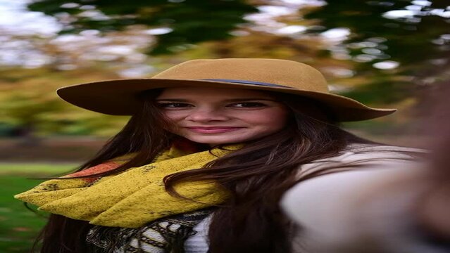 Happy woman with hat looking at camera in autumn in a forest or park. Vertical video.