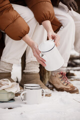 Cropped photo of female holds metal kettle and pours hot drink in big mugs for child. Mom and...