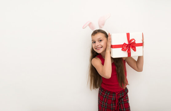  smiling little girl holding gift box on gray background, A beautiful girl with rabbit ears stands and dreams. Christmas gifts concept.
