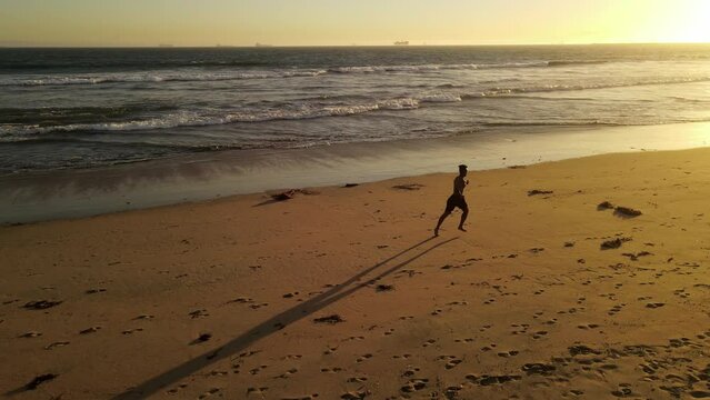 Aerial shot of a Athletic African American Man jogging on the beach at sunset