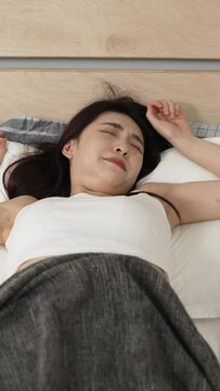 Vertical Screen: asian korean female awaking to sunlight in the morning from sleep is stretching lazily on bed and feeling fatigue in her bed chamber at home.