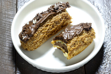 french dessert eclairs with custard and chocolate icing in white plate on wood table