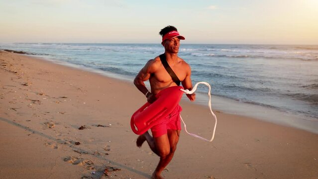 African American lifeguard running along the beach in Southern California at Sunset. Lifeguard's left hand is handicapped.