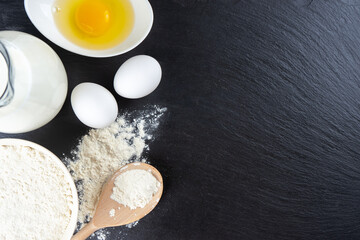 Baking cooking Ingredients background with copy space. Flour, eggs, milk, bakeware on black slate surface. Top view, flat lay. Mockup menu, banner, header for site, baking concept