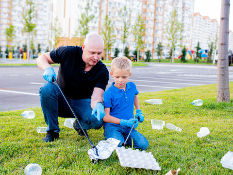 Volunteer dad teaches his son to clean up the trash on the street. Pollution of the environment with plastic and other waste.