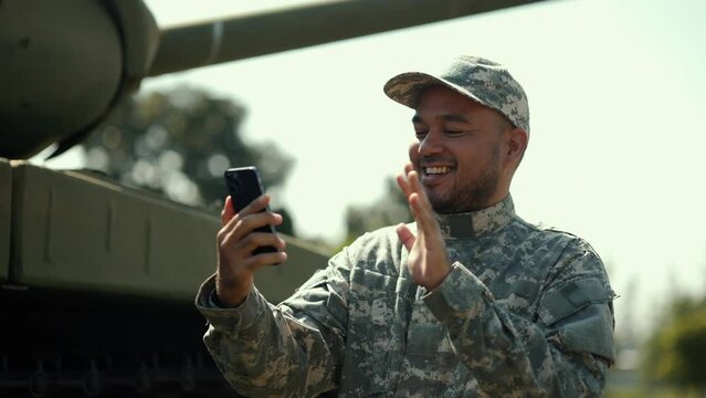 Soldier man in military uniform special forces using smartphone contact your family on field Mission. Army soldier military defender of nation in uniform standing near battle tank while state of war.