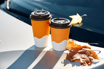 Orange paper coffee cups stand on car illuminated by sun