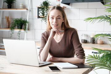 Portrait of a beautiful caucasian young woman looking at the camera. Cute girl with notepad and laptop working or studying at home