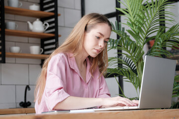 Attractive caucasian girl using computer, looking at device screen and typing. Focused young woman busy working at laptop from home, distance work and education, freelance workday concept
