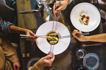 Group of people sharing Chinese steamed dumplings - zenithal view of the table with four hands holding chopsticks on fusion food luxury restaurant