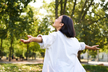 Portrait of carefree young asian woman dancing in park alone, enjoying freedom, smiling with joy