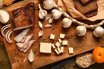 still life of food in a rural style on a dark wood background, sliced lard and garlic, cheese, rye bread and onion, concept of fresh vegetables and healthy food