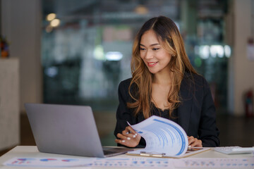 Asian businesswoman sitting happily with her laptop and takes notes intensely and smiles happily at her assignment.