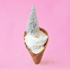 A small snowy Christmas tree on an ice cream cone filled with whipped cream. Minimal surreal concept for winter season holidays advertisement or banner. Creative design for season greetings card.