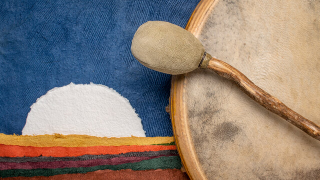 handmade, native American style, shaman drum covered by a goat skin with a beater against abstract paper landscape with a rising moon