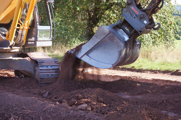 Großer Baggerlöffel schüttet Erdaushub in einen Graben. Die Baustelle ist auf dem Land im...