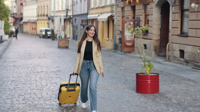 Traveler woman, Carry suitcase, homecoming, vacations. Female tourist walking with suitcase down street in European city, tourism in Europe, pulling luggage down street, young girl traveler walking