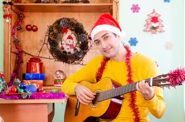 Young cheerful man in Santa hat playing guitar and celebrating Christmas